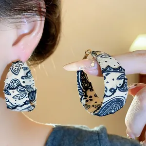 Detail shot of fabric-wrapped hoop earrings featuring black paisley print on beige cloth