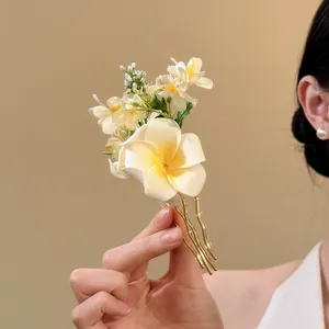 Detail view of an elegant hair fork with white fabric flowers and gold metal prongs.
