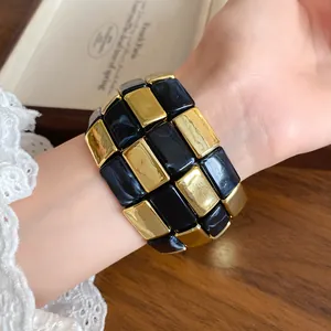 Primo piano di un ampio bracciale in acrilico con blocchi rettangolari neri e dorati.
