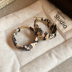 Close-up of stylish fabric-wrapped hoop earrings with black artistic paisley patterns.