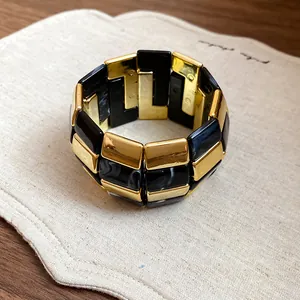 Vista dettagliata del bracciale in acrilico a maglie quadrate marmorizzate nere e oro.
