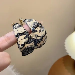 Detailed view of beige paisley print fabric wrapped hoop earrings with silver needle