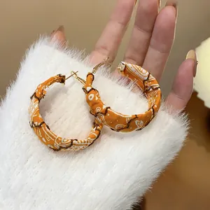 Close-up detail of orange fabric-wrapped hoop earrings with white bohemian paisley pattern