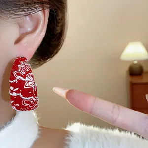 Detailed close-up of a red fabric-covered hoop earring with white patterns worn on ear