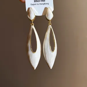 Macro detail view of retro pearlescent white drip oil hollow water drop dangle earrings