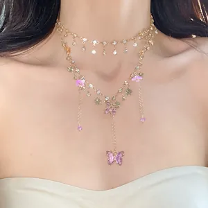 Nahaufnahme einer mehrlagigen Goldkette mit Schmetterlingsanhängern und rosa Steinen