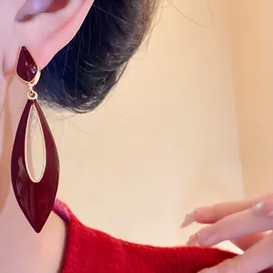 Detail view of burgundy enamel teardrop dangle earrings with gold-tone hollow design