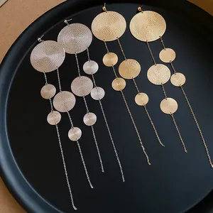 Detailed view of gold and silver textured circular tassel earrings on a black tray