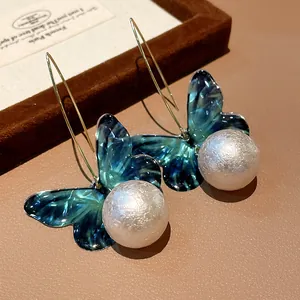 Close-up view of elegant teal marbled butterfly earrings with large lustrous white pearls.