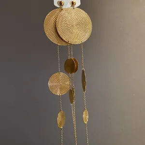Close-up of gold metal earrings with textured circles and long tassel design