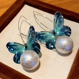 Close-up of elegant butterfly earrings with large pearls and blue-green wings