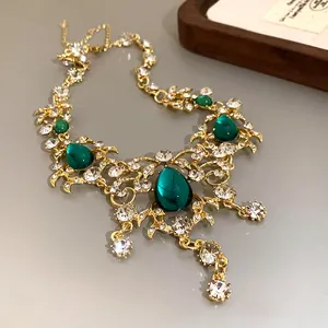 Close-up of vintage gold leaf necklace with emerald green teardrop pendants and crystals.