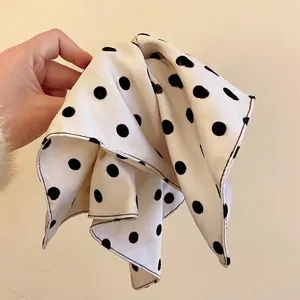 Elegant white fabric hair accessory with black polka dots pattern held by hand