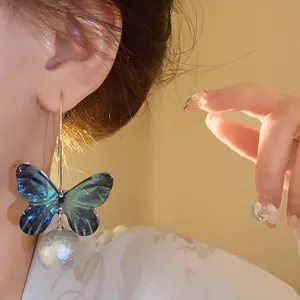 Detailed close-up view of a blue butterfly and pearl drop earring worn on a model's ear