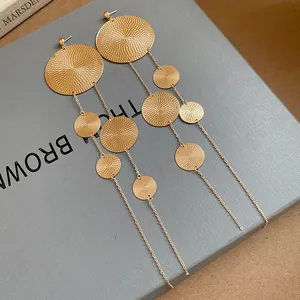 Close-up of gold textured disc tassel earrings with long chains on grey background.