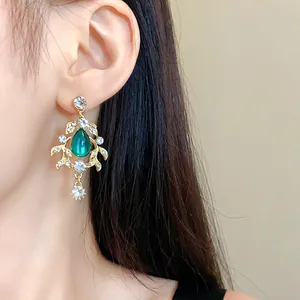 Elegant vintage-style leaf earrings with a green water-drop stone worn on an ear.