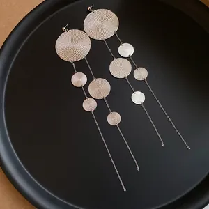 Macro detail of long tassel earrings with concentric circle textures on black tray.