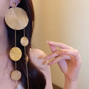 Detailed close-up of oversized gold textured circular disc tassel earrings on model