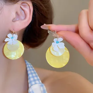 Detailed macro view of white floral drop earrings with yellow pearlescent discs.