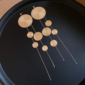 Close-up of golden tassel earrings featuring textured circular discs on black background