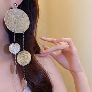 Macro detail of textured metal circular tassel earrings with cascading disc design on model