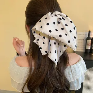 Back view of elegant white polka dot hair bow clip styled on long wavy brunette hair