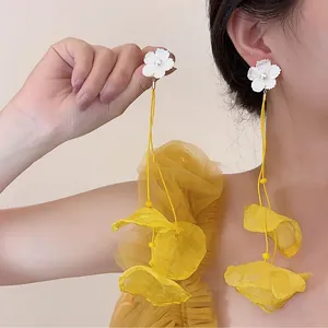Close-up of elegant white flower earrings with long yellow chiffon tassels worn by model