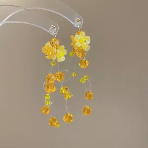 Close-up of yellow floral earrings with tiered faceted bead tassels and silver studs.