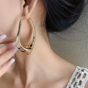 Side view detail of a large gold irregular hollow earring worn by a female model.