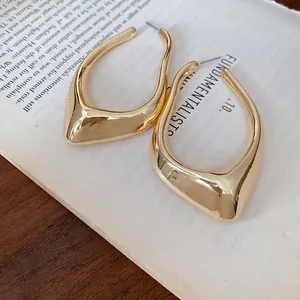 Detailed view of gold irregular geometric U-shaped hoop earrings placed on a book page.