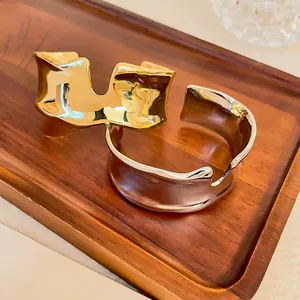 Detail view of gold and silver irregular liquid-style open cuff bracelets on a wood tray