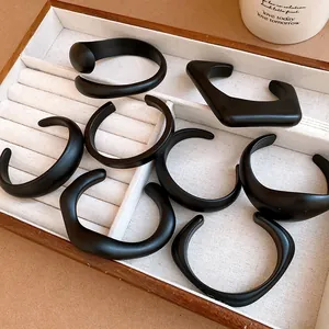 Set of matte black acrylic open cuff bracelets displayed in a wooden jewelry tray