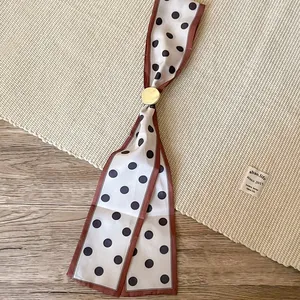 Close-up of a vintage polka dot silk scarf necklace with a golden circular metal buckle.