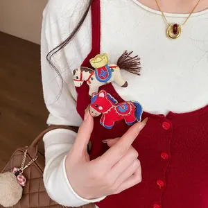 Detailed view of cute embroidered fabric horse brooches pinned on a red knitted vest.