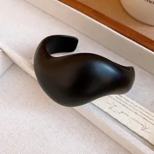 Close-up of minimalist matte black acrylic open cuff bangle with sculptural design.