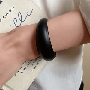Macro detail of a minimalist black acrylic bangle worn on wrist with vintage book background