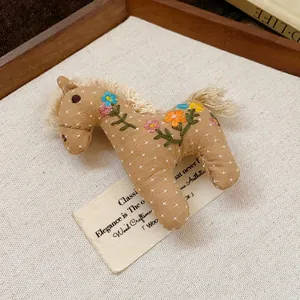 Handmade fabric horse brooch with colorful embroidered flowers on vintage linen background