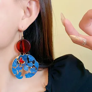 Macro view of New Chinese style enamel flower earrings with a red resin bead on a model