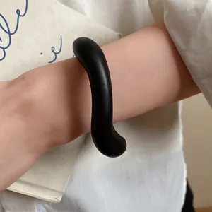 Close-up of a matte black acrylic wavy bangle on wrist with vintage book background