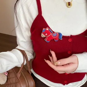 Detail shot of a cute red embroidered fabric horse brooch pinned to a red knitted vest