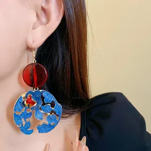 Detailed close-up of vibrant blue enamel flower and red resin bead earrings on model