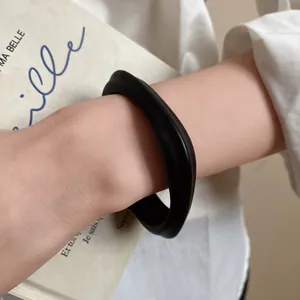 Detail shot of a minimalist matte black acrylic open bangle bracelet on a wrist