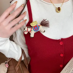 Detail view of cute embroidered fabric horse brooch with gold ingot on red knit vest.