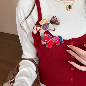 Detail shot of two cute embroidered fabric horse brooches pinned to a red vest