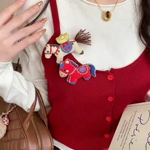 Detailed close-up of cute fabric embroidered horse brooches pinned on a red knit cardigan.