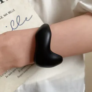 Macro view of a minimalist black matte acrylic open cuff bracelet worn on the wrist