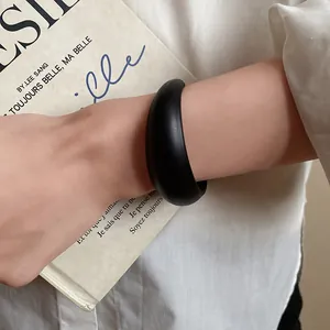 Close-up of minimalist black acrylic open bangle worn on a wrist with a book