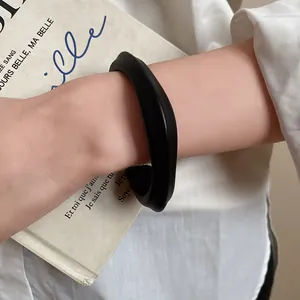 Detail view of a minimalist matte black acrylic open bangle bracelet worn on a wrist.