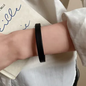 Close-up of a minimalist matte black acrylic open bangle bracelet worn on a female wrist.