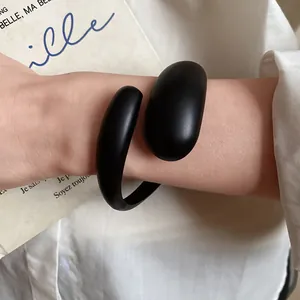 Close-up view of a minimalist black matte acrylic open bracelet worn on a female wrist